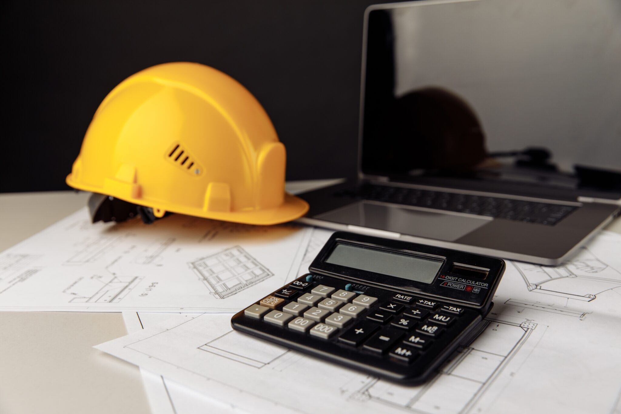Yellow,Helmet,,Calculator,And,Laptop,On,Construction,Plans